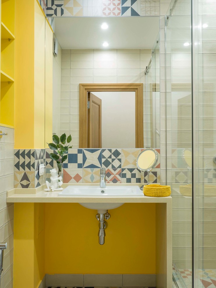 Skandinavisches Duschbad mit gelber Wandfarbe, Einbauwaschbecken, beiger Waschtischplatte, Duschnische, farbigen Fliesen und Schiebetür-Duschabtrennung in Sonstige