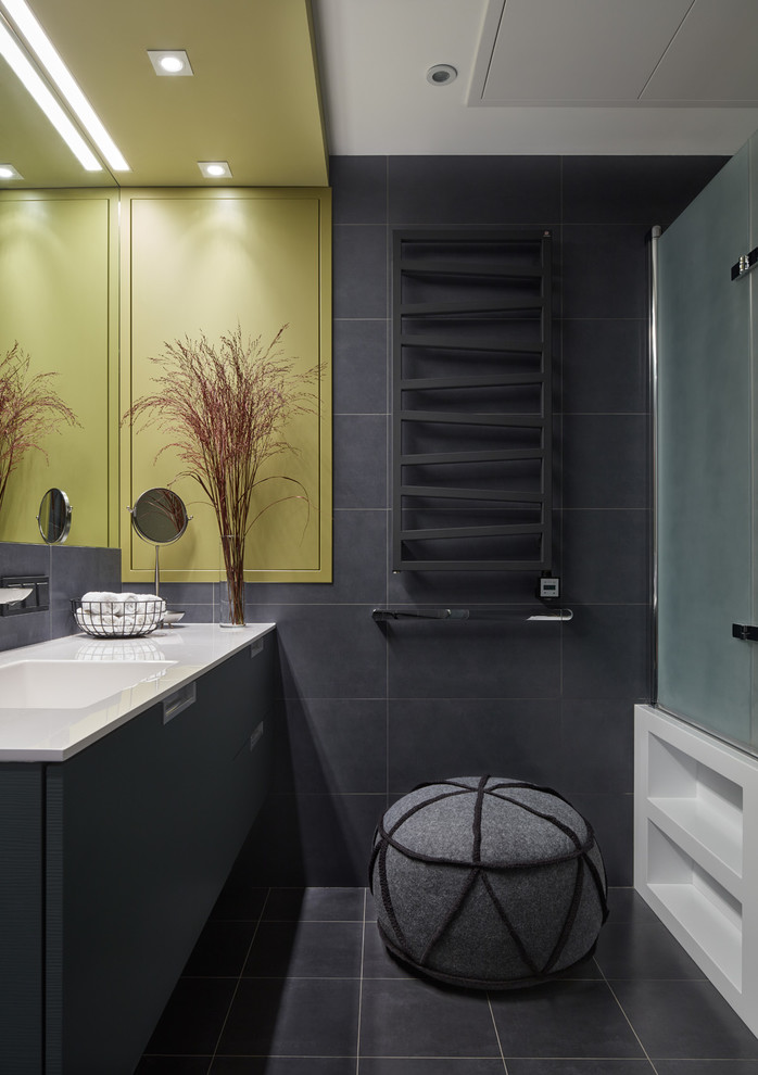 Idée de décoration pour une salle de bain nordique avec un placard à porte plane, des portes de placard grises, un carrelage gris, un mur gris, un lavabo intégré, un plan de toilette en surface solide et une douche d'angle.