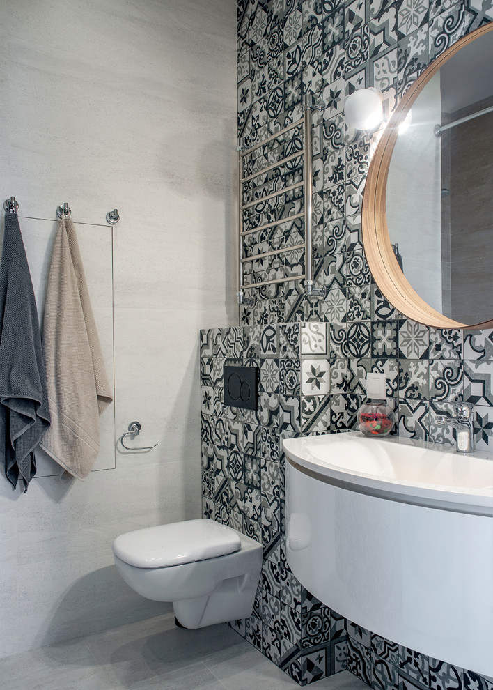 Cette photo montre une salle d'eau scandinave avec des portes de placard blanches, WC suspendus, un carrelage noir et blanc, des carreaux de béton, un mur gris, un lavabo suspendu, un sol gris et un plan de toilette blanc.