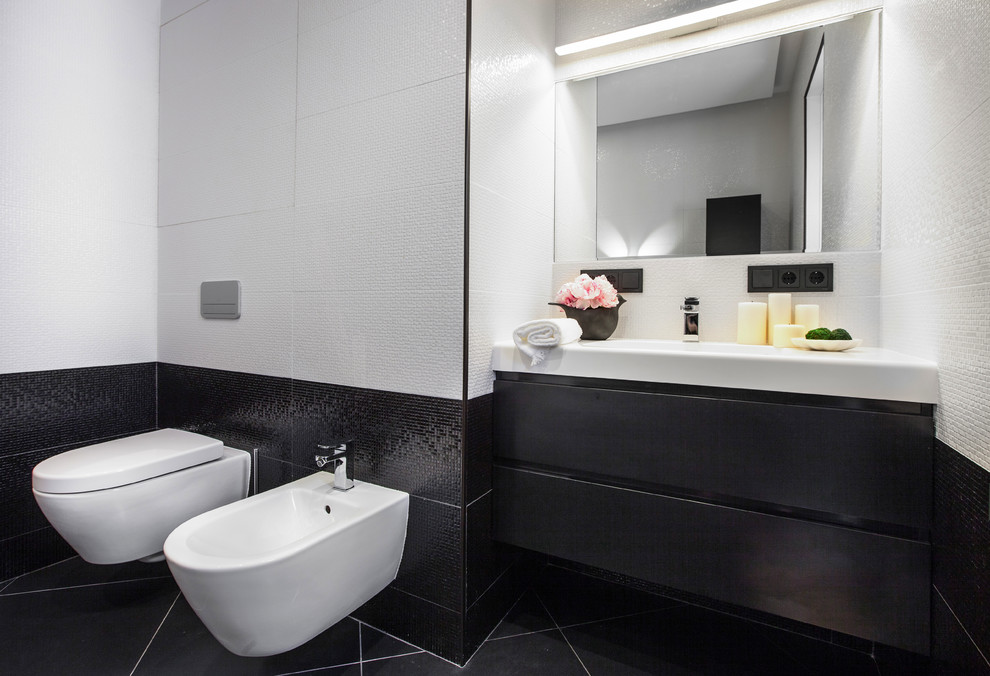 Immagine di una stanza da bagno padronale contemporanea di medie dimensioni con ante lisce, ante nere, piastrelle in ceramica, pavimento in gres porcellanato, top in superficie solida, pavimento nero, bidè, piastrelle bianche, piastrelle nere e lavabo integrato
