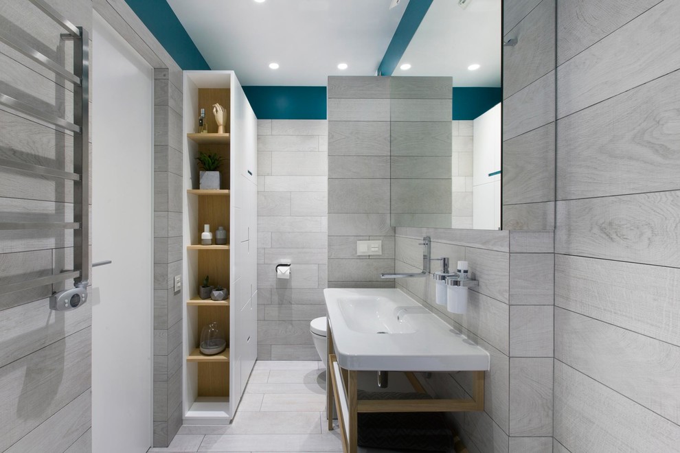 Imagen de cuarto de baño contemporáneo con armarios abiertos, sanitario de pared, baldosas y/o azulejos grises, paredes azules, lavabo tipo consola y suelo gris