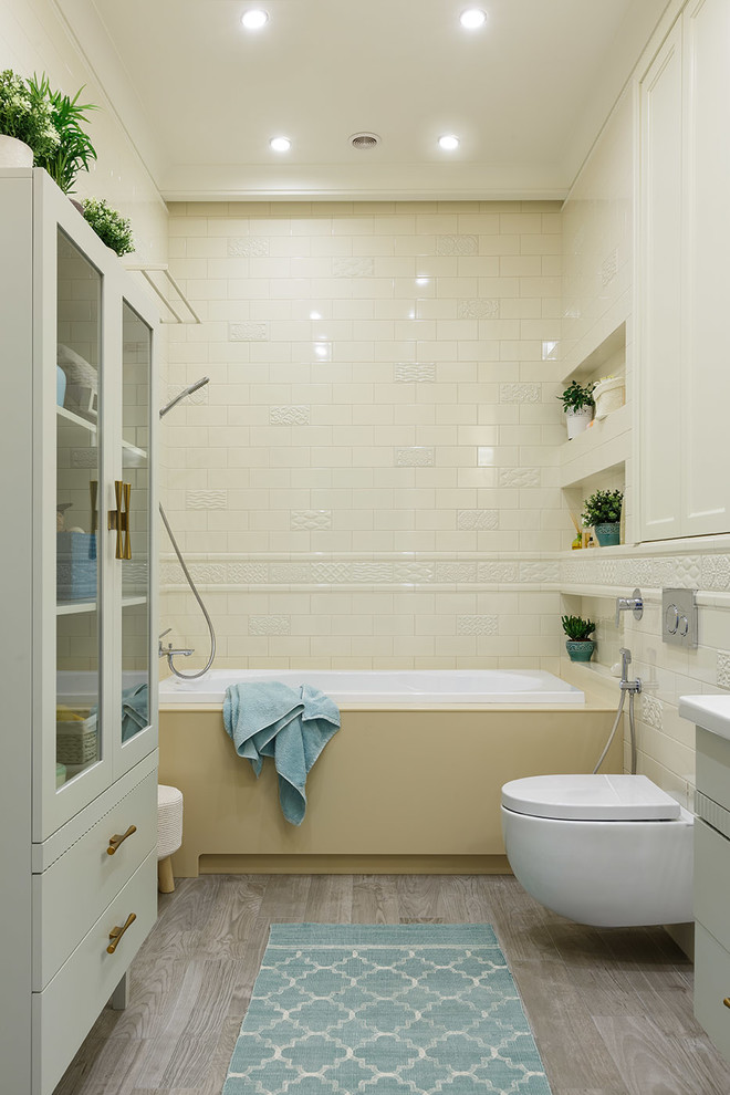 На фото: главная ванная комната среднего размера в стиле неоклассика (современная классика) с плоскими фасадами, серыми фасадами, инсталляцией, белой плиткой, керамической плиткой, желтыми стенами, полом из керамогранита, настольной раковиной, столешницей из искусственного камня, серым полом, накладной ванной и душем над ванной с