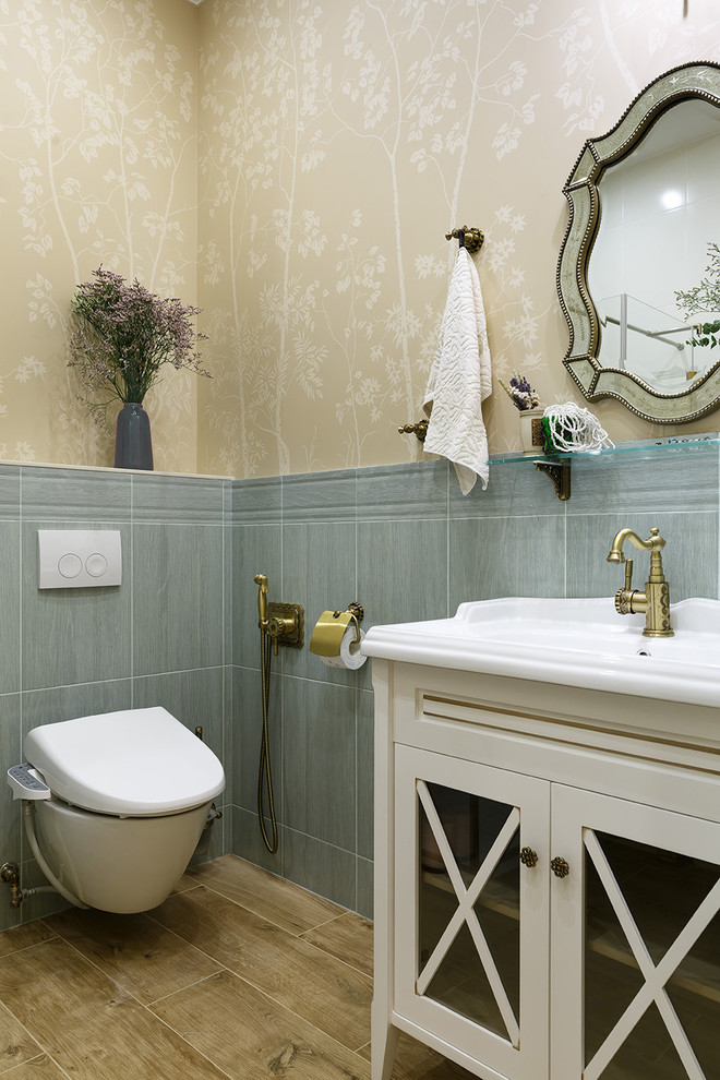 Inredning av ett klassiskt badrum, med luckor med glaspanel, vita skåp, en vägghängd toalettstol, grå kakel, beige väggar, ett integrerad handfat och brunt golv