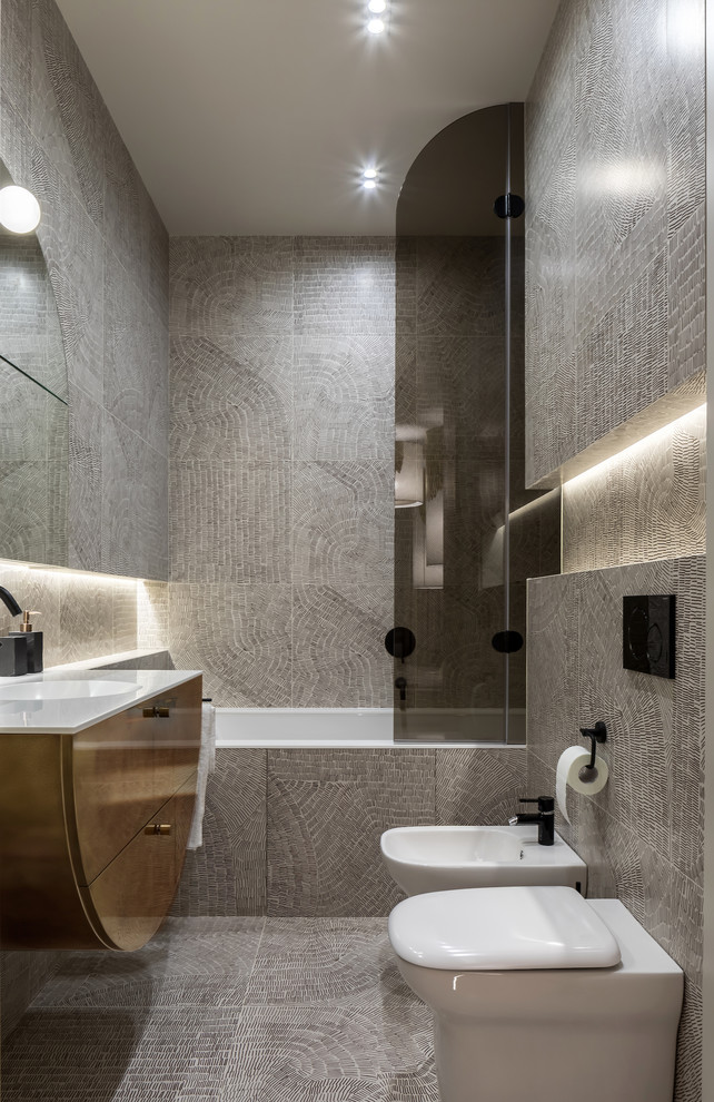 Inredning av ett modernt mellanstort vit vitt en-suite badrum, med släta luckor, gula skåp, ett undermonterat badkar, en dusch i en alkov, en vägghängd toalettstol, grå kakel, keramikplattor, grå väggar, klinkergolv i keramik, ett integrerad handfat, bänkskiva i återvunnet glas, grått golv och dusch med gångjärnsdörr