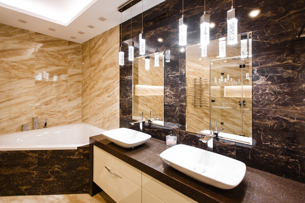 Пример оригинального дизайна: главная ванная комната среднего размера в современном стиле с плоскими фасадами, бежевыми фасадами, угловой ванной, открытым душем, коричневой плиткой, керамогранитной плиткой, накладной раковиной, столешницей из искусственного камня, душем с распашными дверями, коричневой столешницей, инсталляцией, коричневыми стенами, полом из керамогранита и коричневым полом