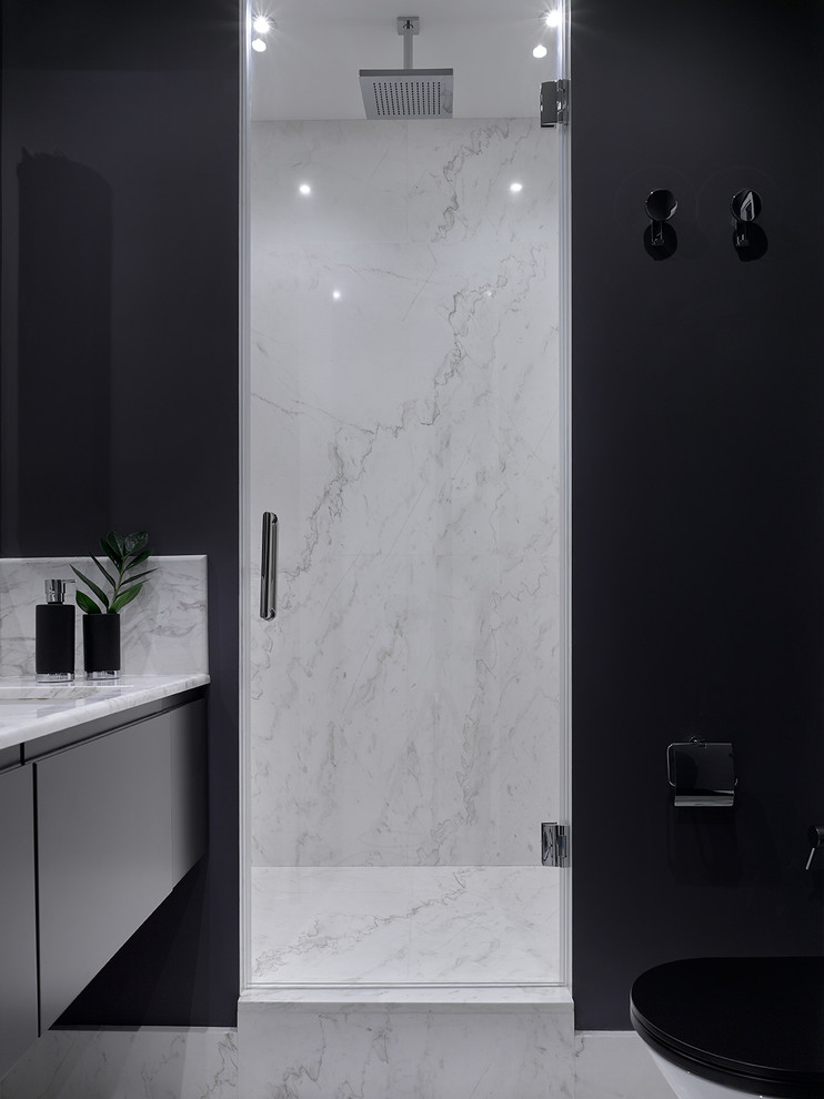 Réalisation d'une salle de bain design avec un lavabo encastré, un plan de toilette en marbre, une cabine de douche à porte battante, un placard à porte plane, un mur gris et des portes de placard noires.