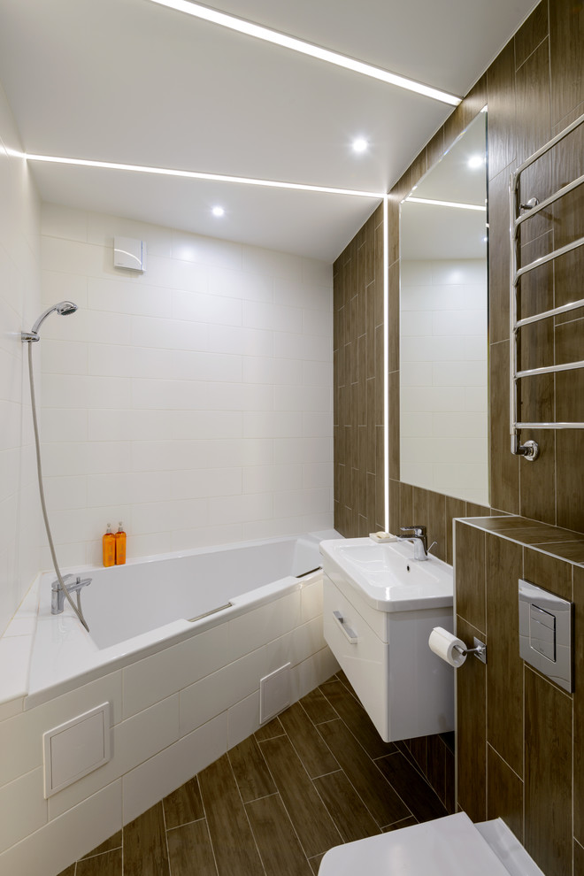Exemple d'une salle de bain principale tendance de taille moyenne avec un placard à porte plane, des portes de placard blanches, une baignoire d'angle, WC suspendus, un carrelage blanc, des carreaux de porcelaine, un mur marron, un sol en carrelage de porcelaine, un lavabo suspendu et un sol marron.