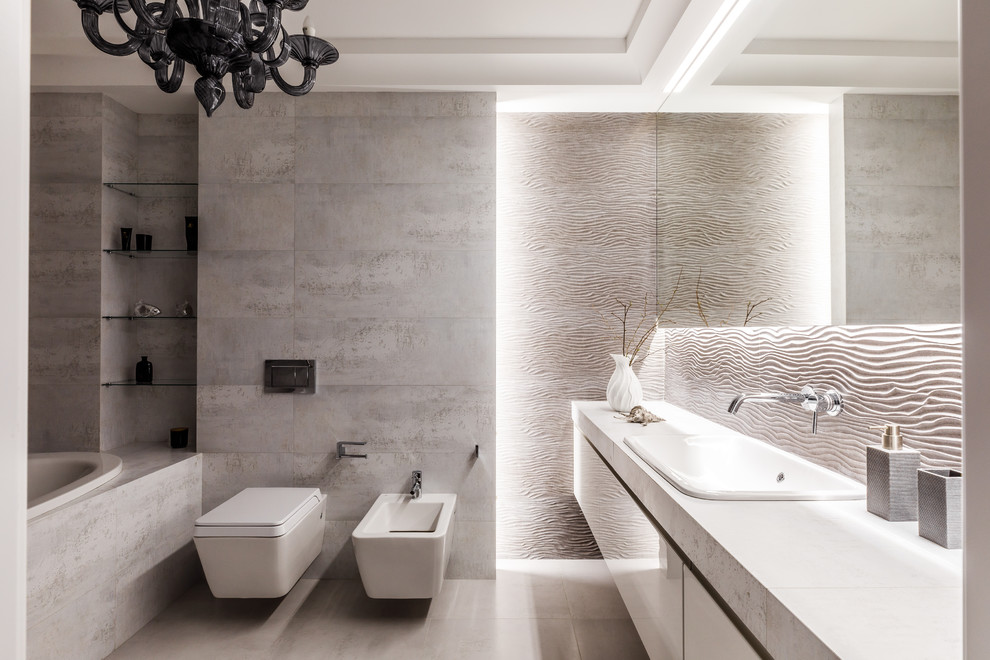 Diseño de cuarto de baño principal actual con armarios con paneles lisos, puertas de armario blancas, bañera encastrada, bidé, baldosas y/o azulejos grises, lavabo encastrado, suelo gris y encimeras blancas