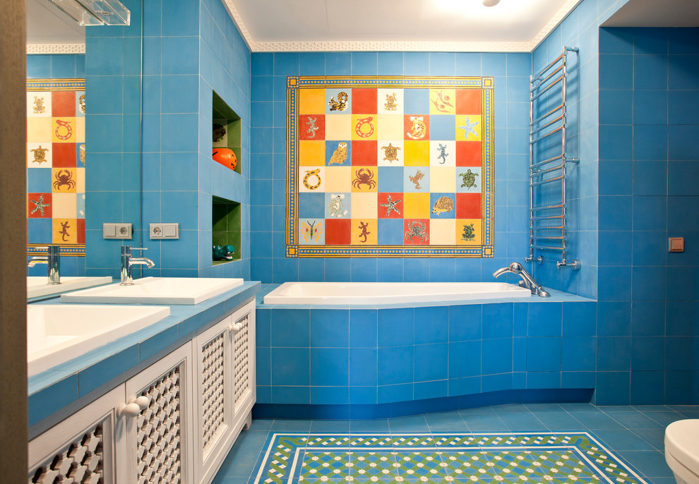 Inredning av ett modernt badrum, med ett badkar i en alkov, blå kakel, flerfärgad kakel och ett nedsänkt handfat