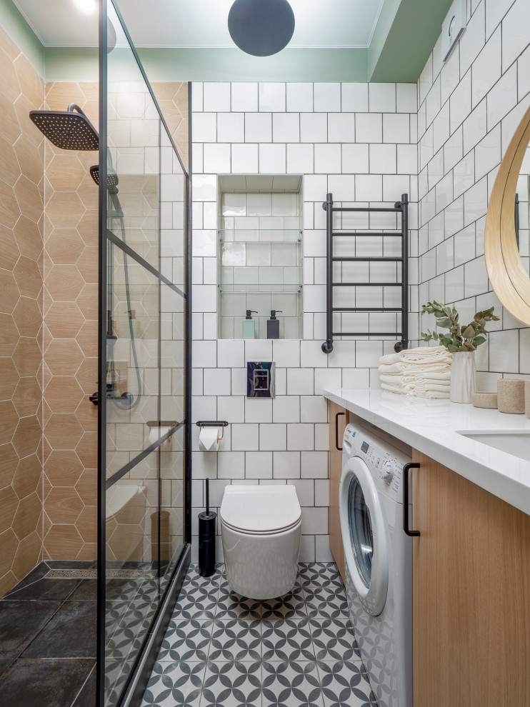 Inredning av ett nordiskt vit vitt badrum med dusch, med släta luckor, skåp i ljust trä, en dusch i en alkov, en vägghängd toalettstol, vit kakel, gröna väggar, ett undermonterad handfat och flerfärgat golv