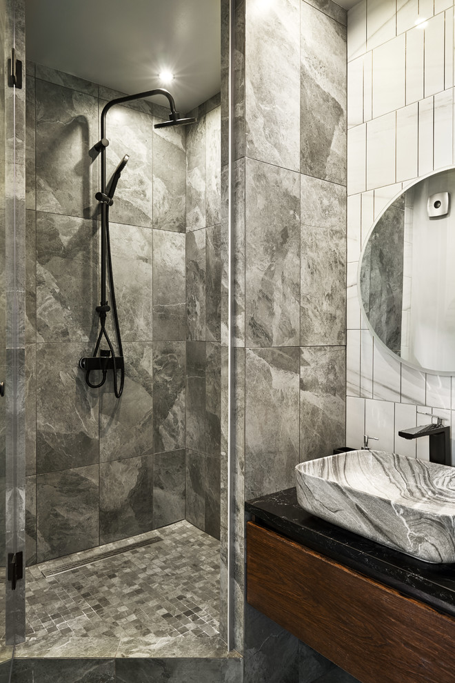 Ejemplo de cuarto de baño contemporáneo con armarios con paneles lisos, puertas de armario de madera en tonos medios, ducha empotrada, baldosas y/o azulejos grises, aseo y ducha, encimeras negras y lavabo sobreencimera