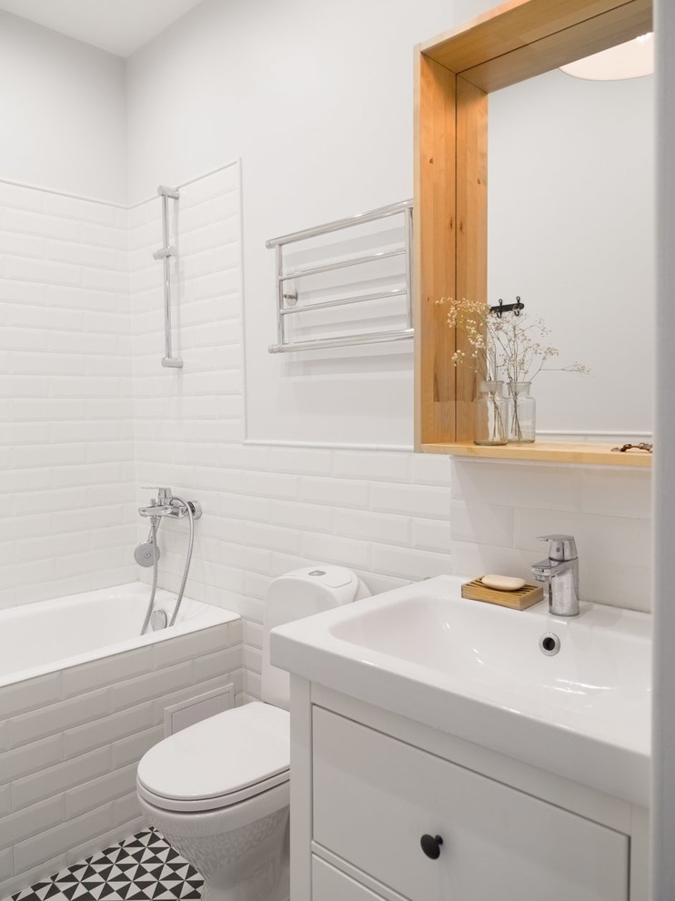 Bild på ett litet skandinaviskt en-suite badrum, med vita skåp, en toalettstol med separat cisternkåpa, vit kakel, keramikplattor, en dusch/badkar-kombination, vita väggar och ett integrerad handfat