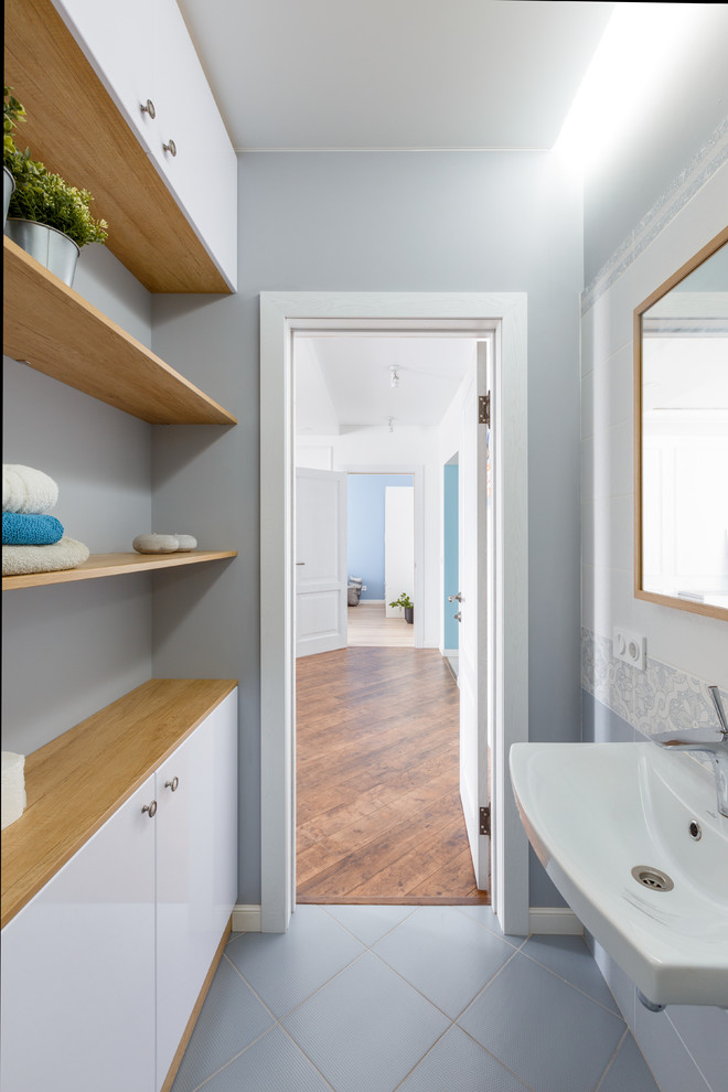 This is an example of a medium sized bohemian shower room bathroom in Novosibirsk with flat-panel cabinets, white cabinets, an alcove shower, a wall mounted toilet, grey tiles, ceramic tiles, grey walls, ceramic flooring, a wall-mounted sink, grey floors and a hinged door.