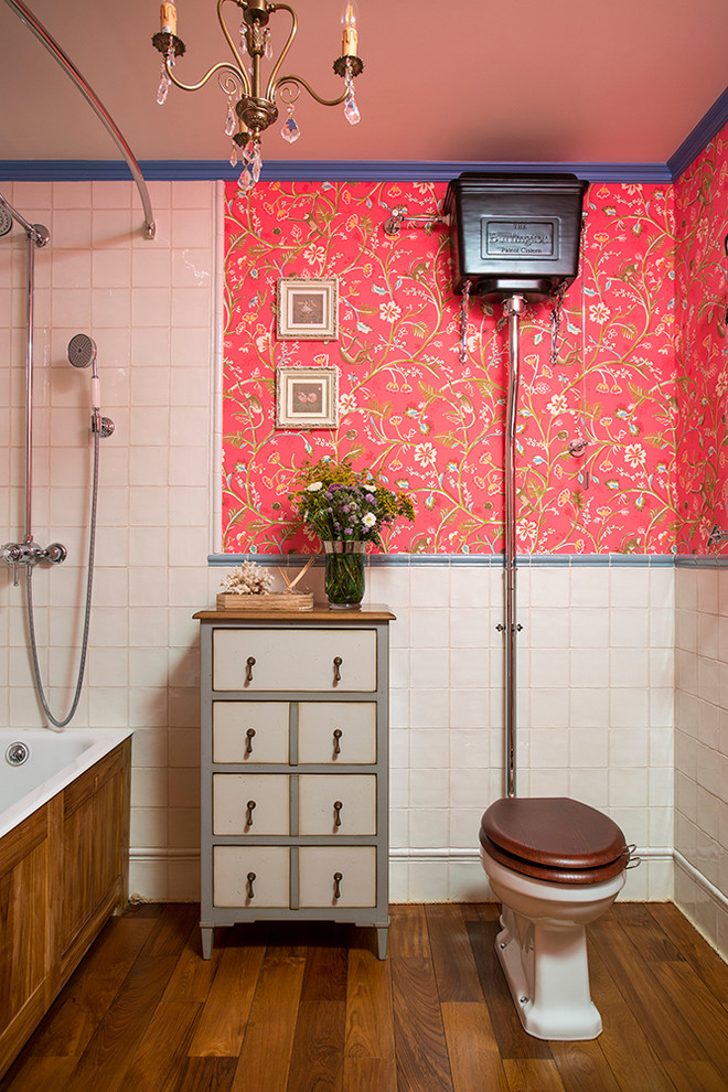 Bild på ett mellanstort vintage badrum för barn, med skåp i slitet trä, ett badkar i en alkov, en dusch/badkar-kombination, vit kakel, släta luckor, en toalettstol med separat cisternkåpa, röda väggar, mörkt trägolv och dusch med duschdraperi