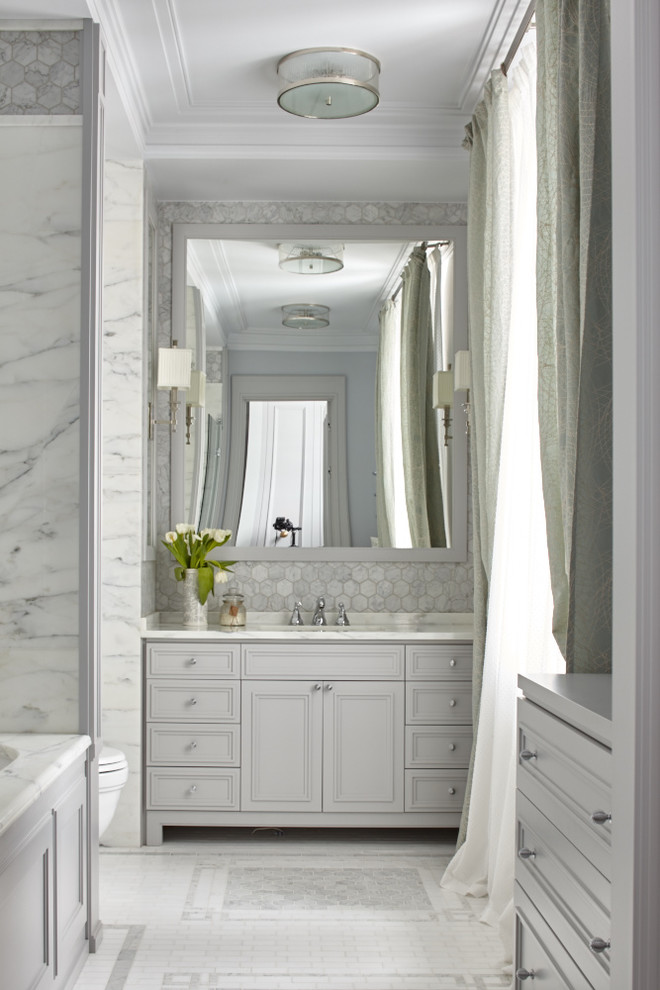 Klassisk inredning av ett en-suite badrum, med luckor med infälld panel, grå skåp, ett badkar i en alkov, grå kakel, stenkakel, ett undermonterad handfat, marmorbänkskiva och en dusch/badkar-kombination