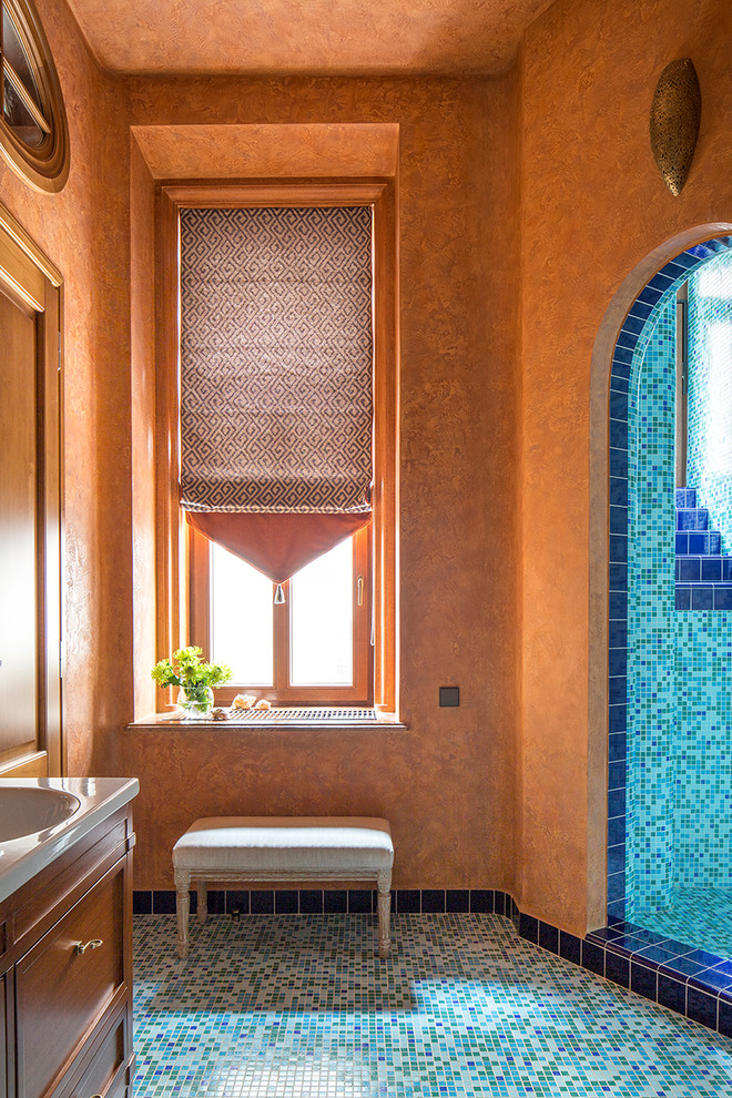 Пример оригинального дизайна: ванная комната в средиземноморском стиле с фасадами с утопленной филенкой, фасадами цвета дерева среднего тона, синей плиткой, плиткой мозаикой, оранжевыми стенами, полом из мозаичной плитки, душевой кабиной, монолитной раковиной и душем в нише