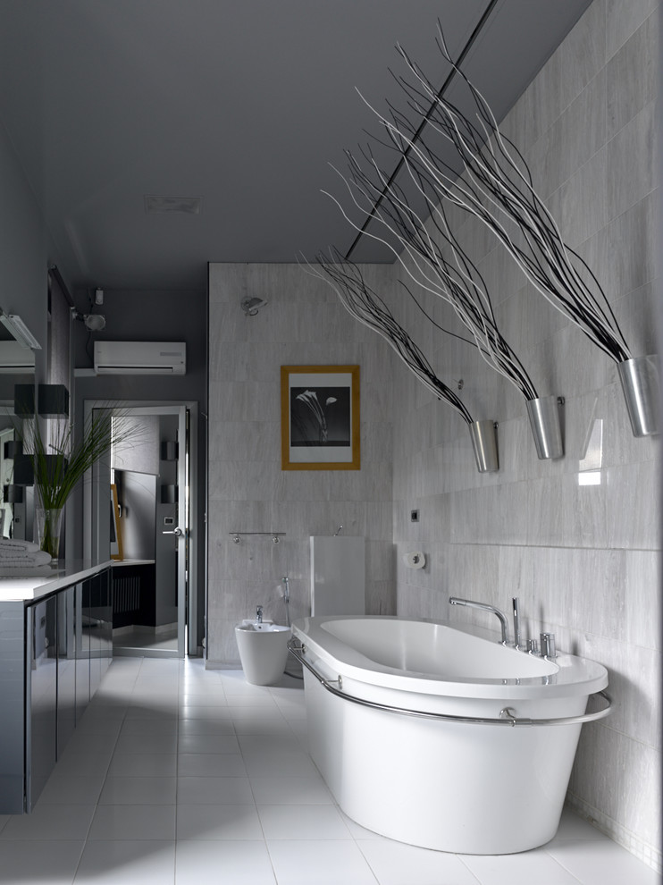 Cette image montre une salle de bain principale design avec un placard à porte plane, une baignoire indépendante, un carrelage gris et un sol blanc.