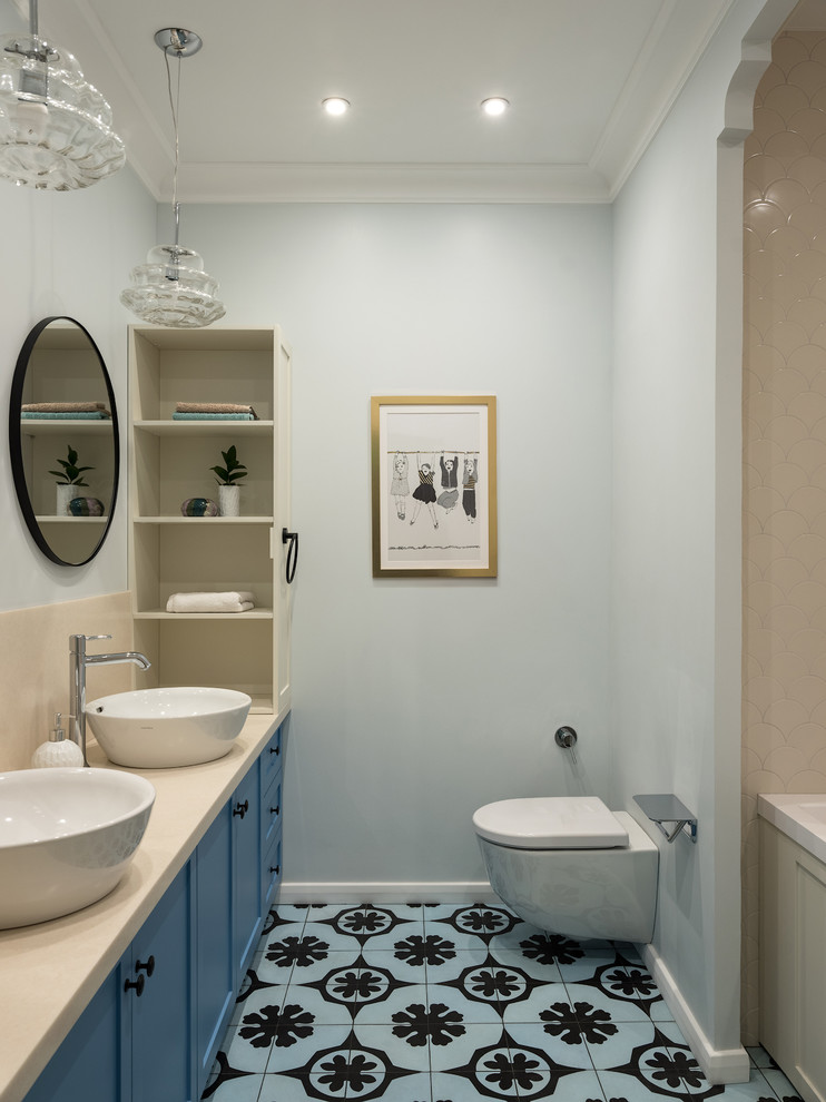 Cette image montre une petite salle de bain principale traditionnelle avec un placard avec porte à panneau encastré, des portes de placard bleues, une baignoire encastrée, WC suspendus, un carrelage beige, des carreaux de céramique, un mur bleu, carreaux de ciment au sol, un lavabo posé, un plan de toilette en surface solide, un sol bleu et un plan de toilette beige.