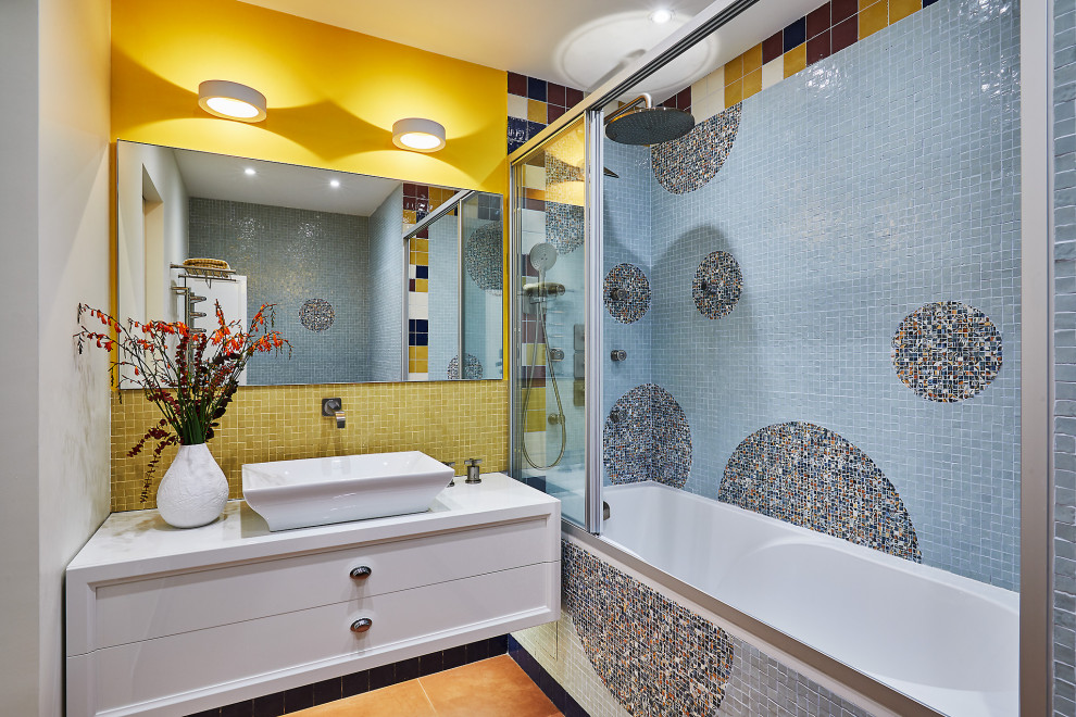 На фото: ванная комната среднего размера в современном стиле с фасадами с утопленной филенкой, белыми фасадами, ванной в нише, душем над ванной, синей плиткой, разноцветной плиткой, желтой плиткой, желтыми стенами, душевой кабиной, настольной раковиной, оранжевым полом, душем с раздвижными дверями и белой столешницей с