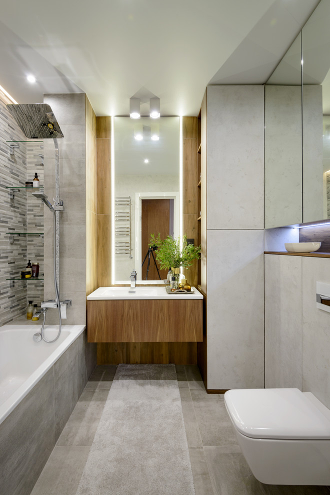 Идея дизайна: главная ванная комната в современном стиле с плоскими фасадами, фасадами цвета дерева среднего тона, ванной в нише, душем над ванной, инсталляцией, серой плиткой, серым полом, белой столешницей, серыми стенами и подвесной раковиной