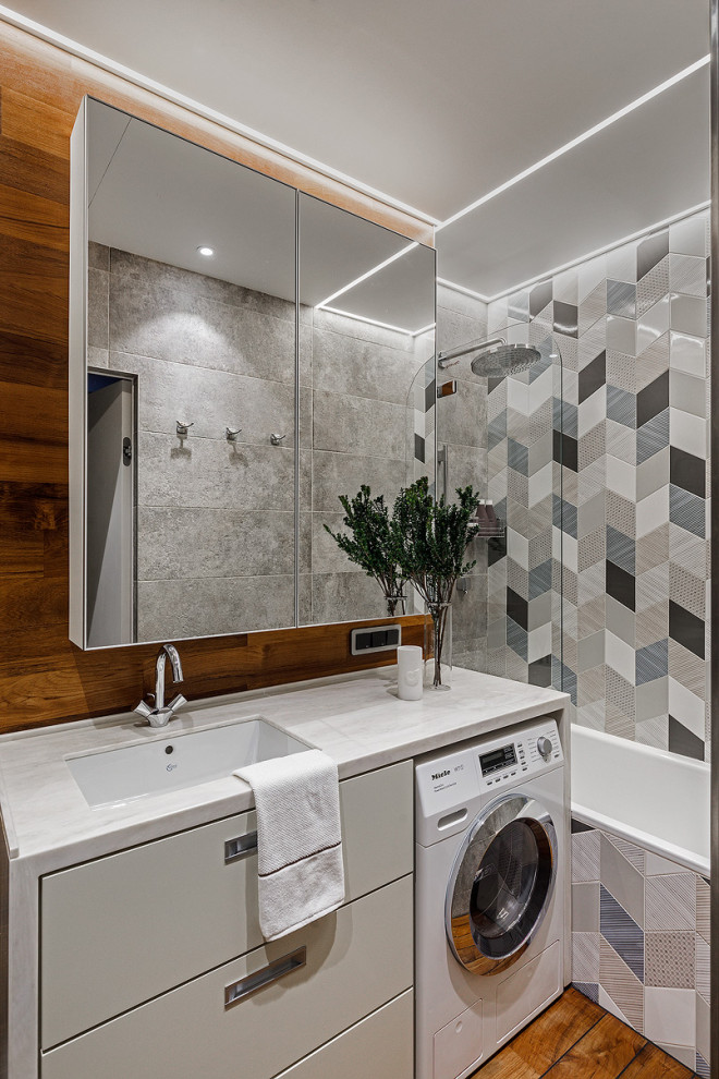 Bild på ett mellanstort funkis vit vitt badrum, med vita skåp, ett badkar i en alkov, ett undermonterad handfat, brunt golv, en dusch/badkar-kombination, mellanmörkt trägolv, släta luckor, en vägghängd toalettstol, grå kakel, porslinskakel, flerfärgade väggar och bänkskiva i kvarts