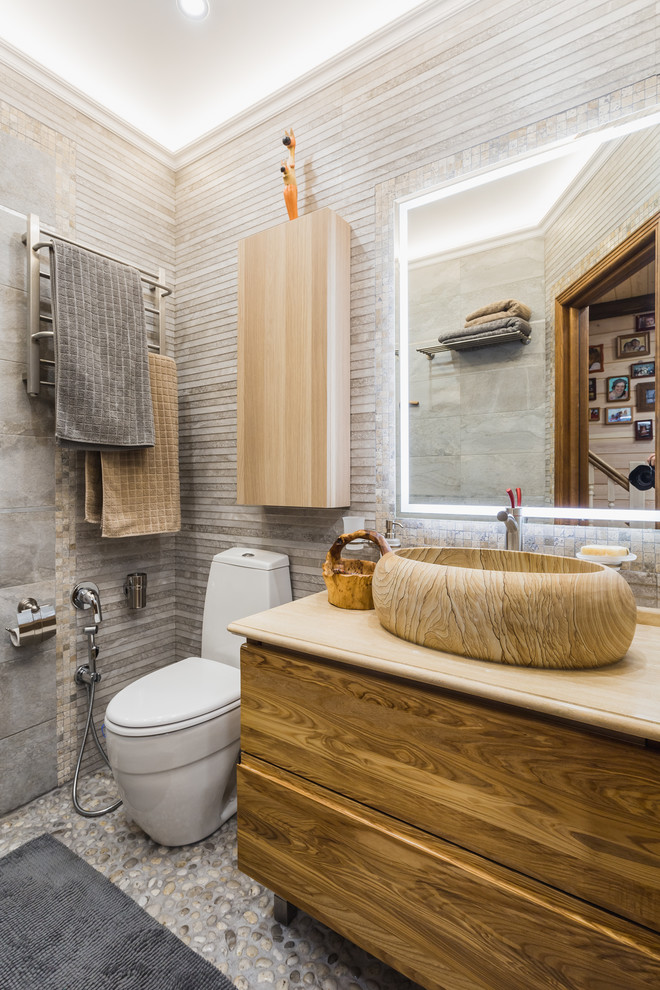 Modernes Duschbad mit flächenbündigen Schrankfronten, hellbraunen Holzschränken, Wandtoilette mit Spülkasten, grauen Fliesen, Kiesel-Bodenfliesen und Aufsatzwaschbecken in Moskau
