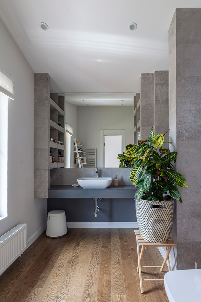 Diseño de cuarto de baño contemporáneo con baldosas y/o azulejos grises, paredes grises, suelo de madera en tonos medios, lavabo sobreencimera, suelo marrón y encimeras grises