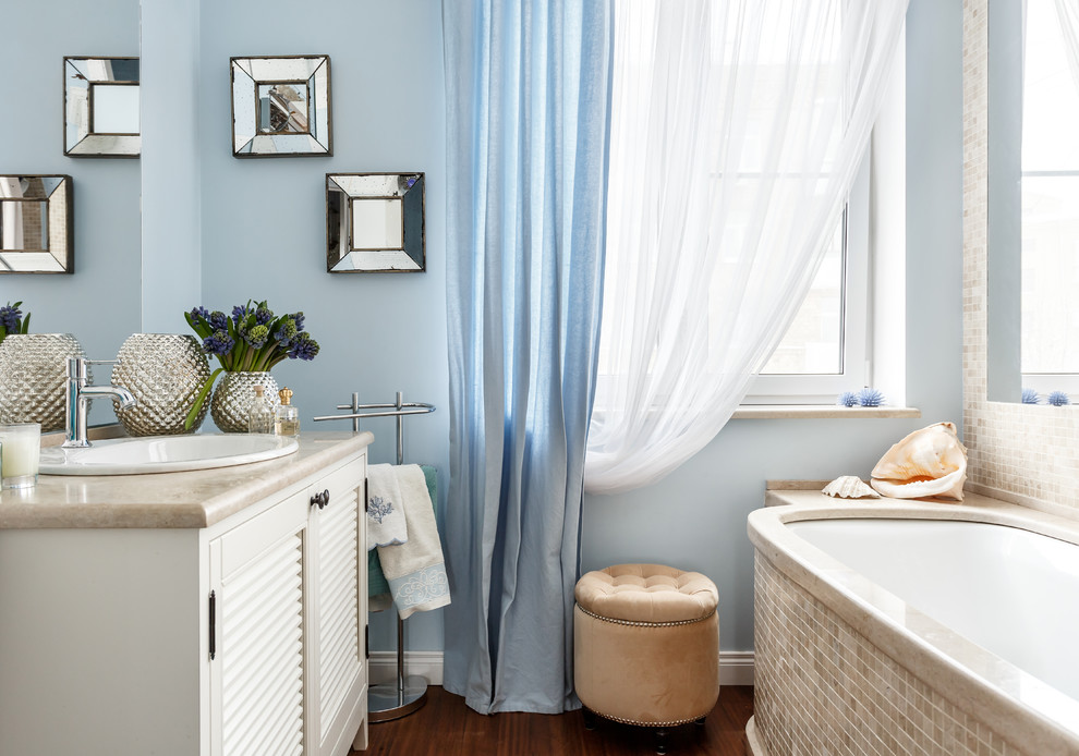 Свежая идея для дизайна: главная ванная комната в морском стиле с фасадами с филенкой типа жалюзи, белыми фасадами, полновстраиваемой ванной, бежевой плиткой, плиткой мозаикой, синими стенами, накладной раковиной, коричневым полом, бежевой столешницей и столешницей из известняка - отличное фото интерьера