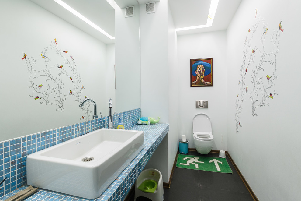Imagen de cuarto de baño actual con lavabo sobreencimera, sanitario de pared, baldosas y/o azulejos azules, baldosas y/o azulejos en mosaico, paredes blancas y encimera de azulejos