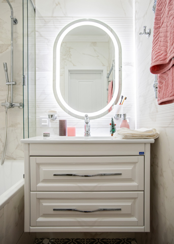 На фото: главная ванная комната в современном стиле с белыми фасадами, душем над ванной, белой столешницей, фасадами с выступающей филенкой, ванной в нише, монолитной раковиной, душем с раздвижными дверями и зеркалом с подсветкой