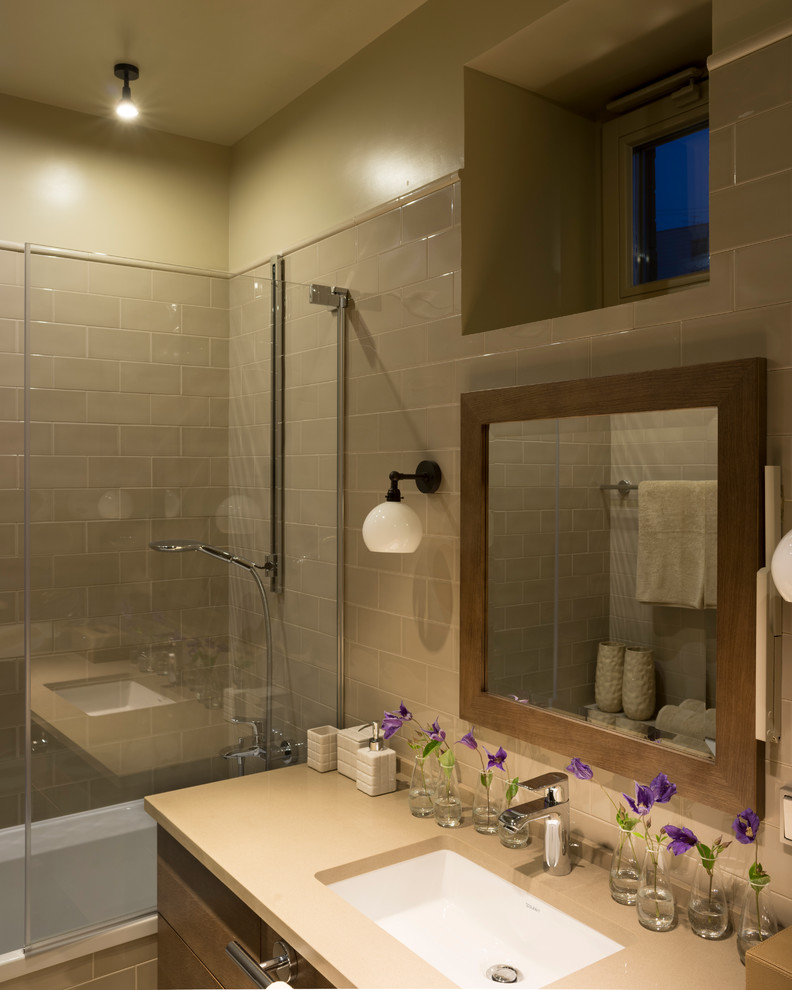 Bild på ett mellanstort funkis badrum, med beige kakel, beige väggar, bänkskiva i kvarts, ett undermonterad handfat, skåp i mellenmörkt trä, en dusch/badkar-kombination och släta luckor