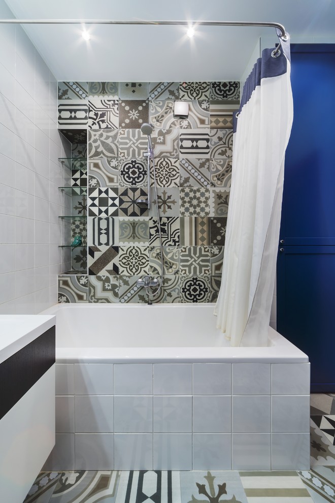 Exemple d'une salle de bain principale tendance de taille moyenne avec une cabine de douche avec un rideau, un placard avec porte à panneau surélevé, des portes de placard bleues, une baignoire en alcôve, WC suspendus, un carrelage gris, des carreaux de porcelaine, un mur blanc, un sol en carrelage de porcelaine, un lavabo encastré, un plan de toilette en surface solide et un sol gris.