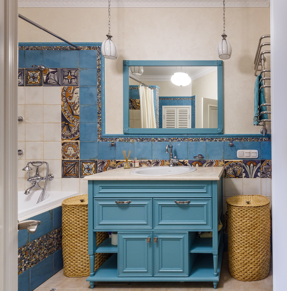 他の地域にある地中海スタイルのおしゃれなマスターバスルーム (落し込みパネル扉のキャビネット、青いキャビネット、アルコーブ型浴槽、青いタイル、マルチカラーのタイル、ベージュの壁、オーバーカウンターシンク、ベージュの床) の写真