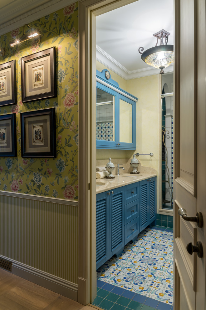 Идея дизайна: большая ванная комната в средиземноморском стиле с фасадами с филенкой типа жалюзи, синими фасадами, душем в нише, керамогранитной плиткой, желтыми стенами, полом из керамогранита, врезной раковиной, мраморной столешницей, разноцветным полом и бежевой столешницей