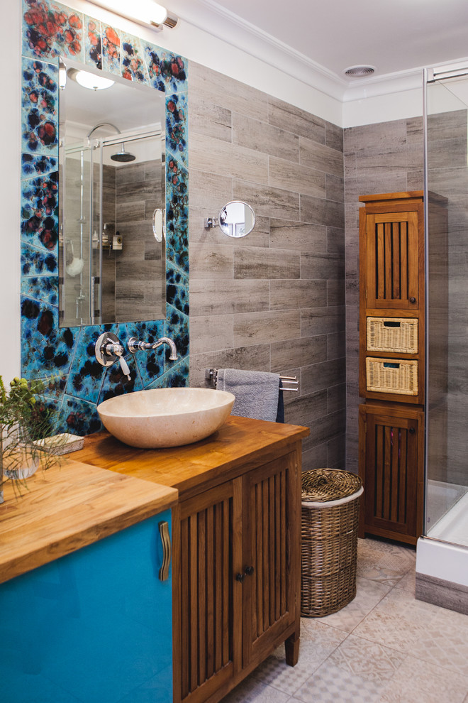 Diseño de cuarto de baño ecléctico con puertas de armario de madera oscura, ducha esquinera, baldosas y/o azulejos grises y lavabo sobreencimera