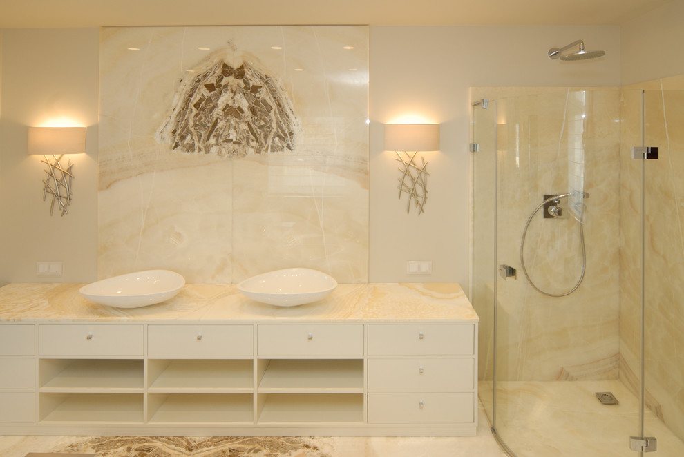 Пример оригинального дизайна: огромная ванная комната в классическом стиле с фасадами островного типа, бежевыми фасадами, полновстраиваемой ванной, открытым душем, инсталляцией, бежевой плиткой, мраморной плиткой, бежевыми стенами, мраморным полом, душевой кабиной, настольной раковиной, столешницей из оникса, бежевым полом, душем с распашными дверями и белой столешницей