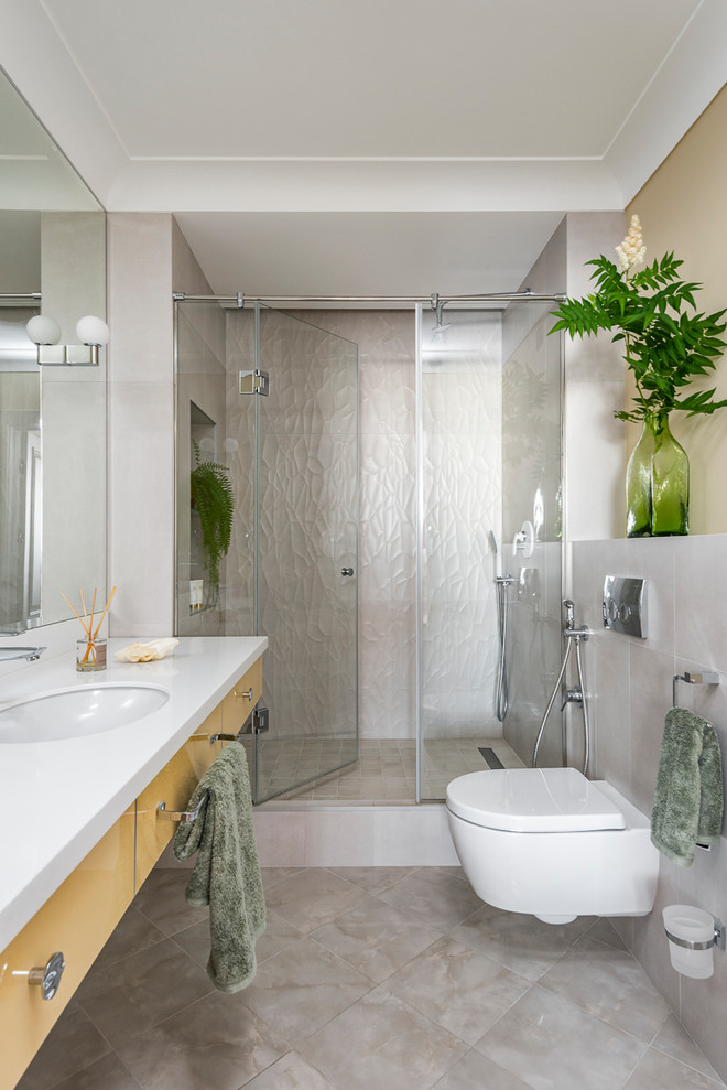 Inredning av ett modernt mellanstort vit vitt badrum med dusch, med släta luckor, gula skåp, en dusch i en alkov, en vägghängd toalettstol, ett undermonterad handfat, bänkskiva i akrylsten, dusch med gångjärnsdörr, grå kakel och grått golv