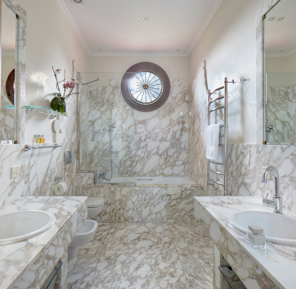 Cette image montre une salle d'eau design de taille moyenne avec du carrelage en marbre, un sol en marbre, des portes de placard beiges, une baignoire en alcôve, un combiné douche/baignoire, un carrelage beige, un mur beige, un lavabo posé, un sol beige et un plan de toilette beige.