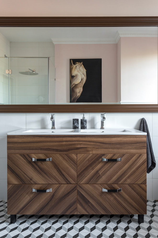 Inredning av ett modernt badrum, med släta luckor, skåp i mörkt trä, en hörndusch, vit kakel, rosa väggar, ett avlångt handfat och flerfärgat golv