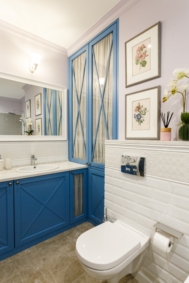 Idéer för att renovera ett mellanstort vintage vit vitt en-suite badrum, med luckor med glaspanel, blå skåp, ett undermonterat badkar, en dusch/badkar-kombination, en vägghängd toalettstol, vit kakel, keramikplattor, grå väggar, klinkergolv i keramik, ett undermonterad handfat, bänkskiva i kvarts och grått golv