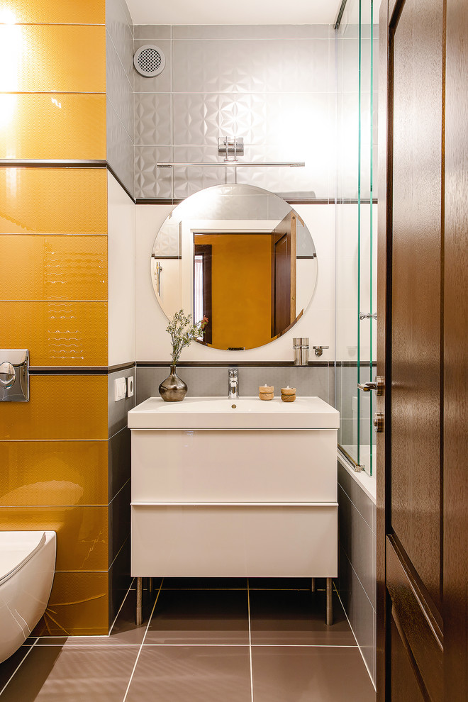 Idéer för att renovera ett funkis en-suite badrum, med släta luckor, vita skåp, ett badkar i en alkov, en dusch/badkar-kombination, en vägghängd toalettstol, vit kakel, gul kakel, grå kakel, ett integrerad handfat och brunt golv