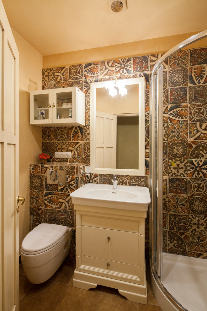 Modelo de cuarto de baño actual con puertas de armario blancas, ducha esquinera, sanitario de pared, baldosas y/o azulejos marrones y lavabo encastrado