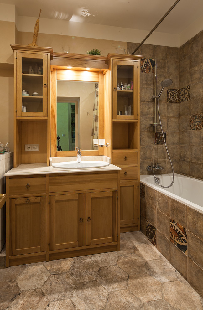 На фото: главная ванная комната в стиле кантри с фасадами в стиле шейкер, фасадами цвета дерева среднего тона, ванной в нише, душем над ванной, бежевой плиткой, бежевыми стенами, накладной раковиной и шторкой для ванной