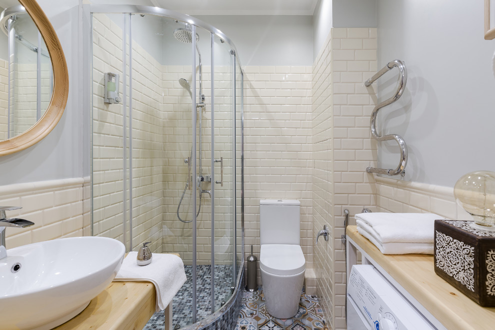 Inredning av ett eklektiskt litet badrum med dusch, med öppna hyllor, skåp i ljust trä, en hörndusch, en vägghängd toalettstol, beige kakel, tunnelbanekakel, grå väggar, cementgolv, ett fristående handfat, träbänkskiva, flerfärgat golv och dusch med skjutdörr