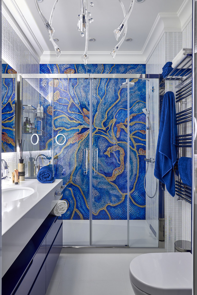 Idée de décoration pour une salle de bain design avec un placard à porte plane, des portes de placard bleues, un carrelage multicolore, mosaïque, un lavabo encastré, un sol blanc, une cabine de douche à porte coulissante et un plan de toilette blanc.