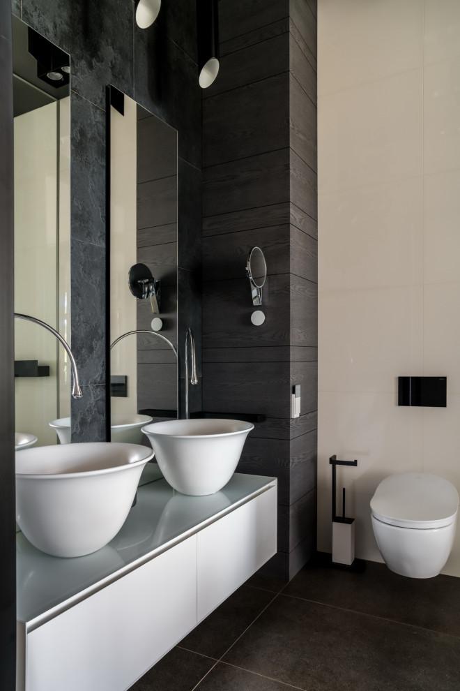 Cette image montre une salle de bain design de taille moyenne avec un placard à porte plane, des portes de placard grises, WC suspendus, un carrelage beige, un carrelage gris, une vasque, un sol noir, un plan de toilette gris, meuble double vasque et meuble-lavabo suspendu.