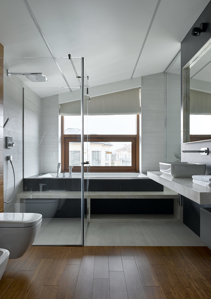 Diseño de cuarto de baño principal contemporáneo con bañera encastrada, sanitario de pared, baldosas y/o azulejos grises, lavabo sobreencimera, suelo marrón, ducha con puerta con bisagras y ventanas