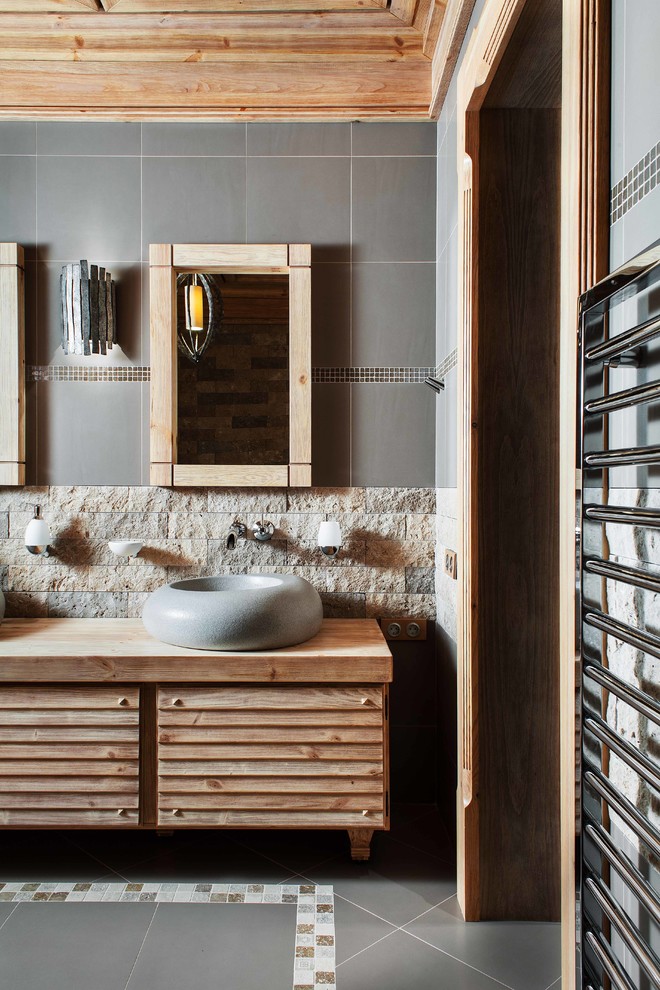 Идея дизайна: ванная комната в стиле рустика с фасадами с филенкой типа жалюзи, фасадами цвета дерева среднего тона, серой плиткой, настольной раковиной и столешницей из дерева