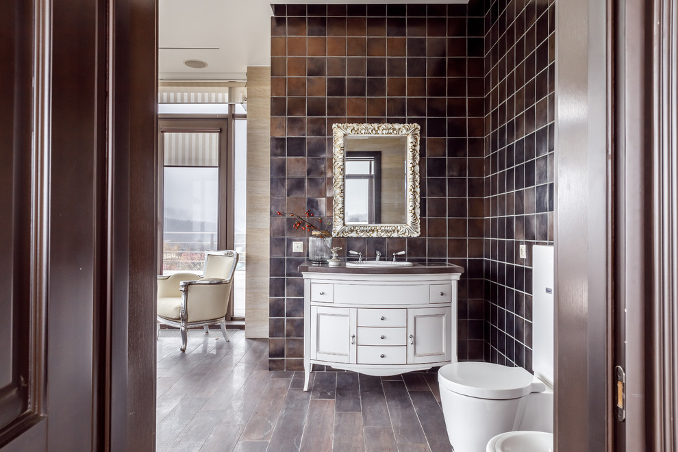 Стильный дизайн: ванная комната в стиле неоклассика (современная классика) с белыми фасадами, раздельным унитазом, коричневой плиткой, накладной раковиной, коричневой столешницей, фасадами в стиле шейкер и коричневым полом - последний тренд