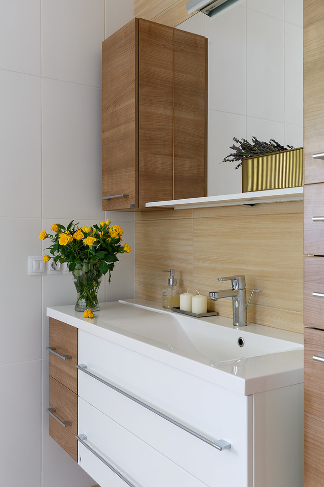 На фото: ванная комната в современном стиле с плоскими фасадами, фасадами цвета дерева среднего тона, белой плиткой и монолитной раковиной